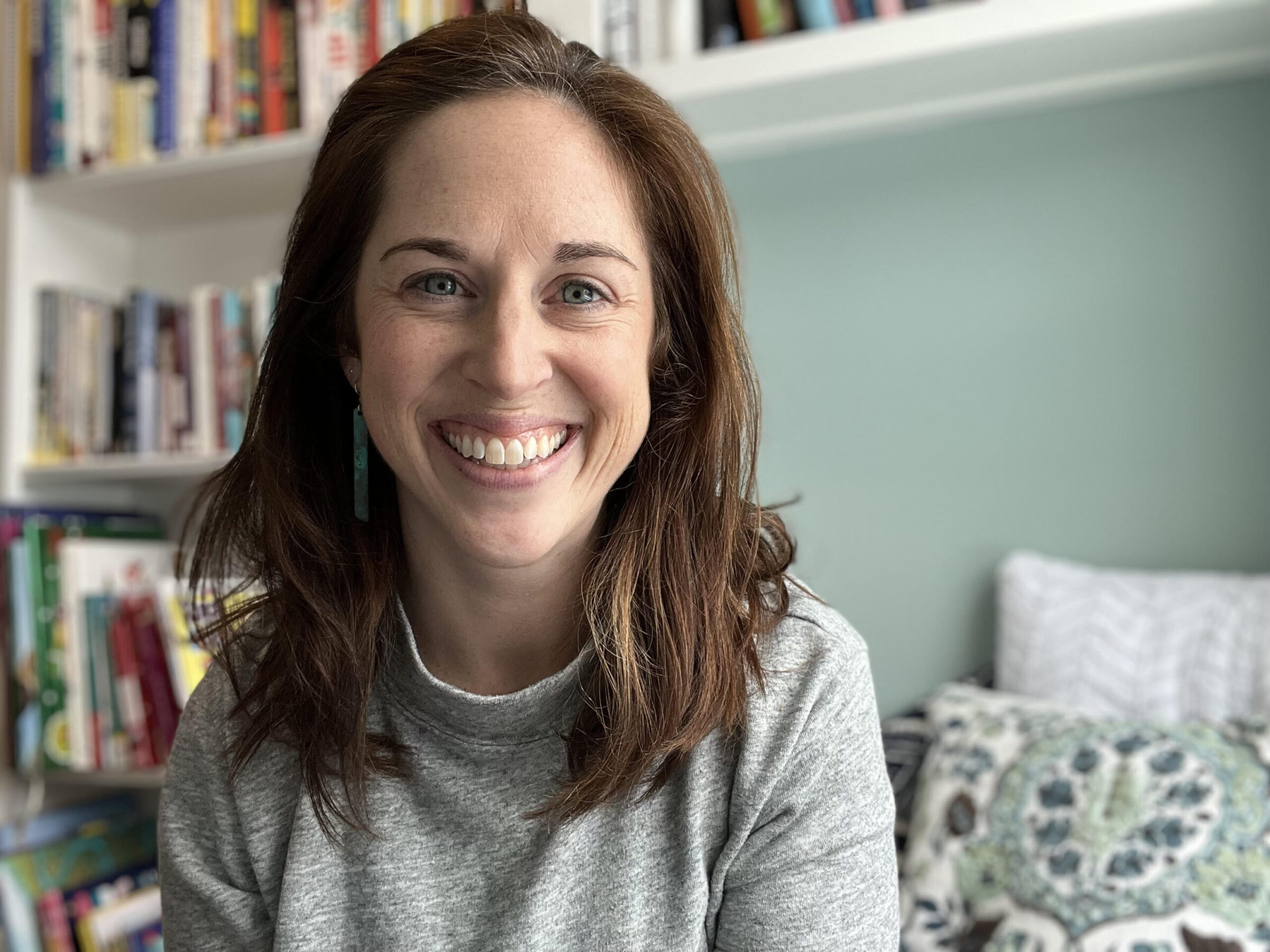 Smiling woman in a cozy counseling setting, surrounded by books, representing compassionate support for grief and loss at Maine Tides Counseling.